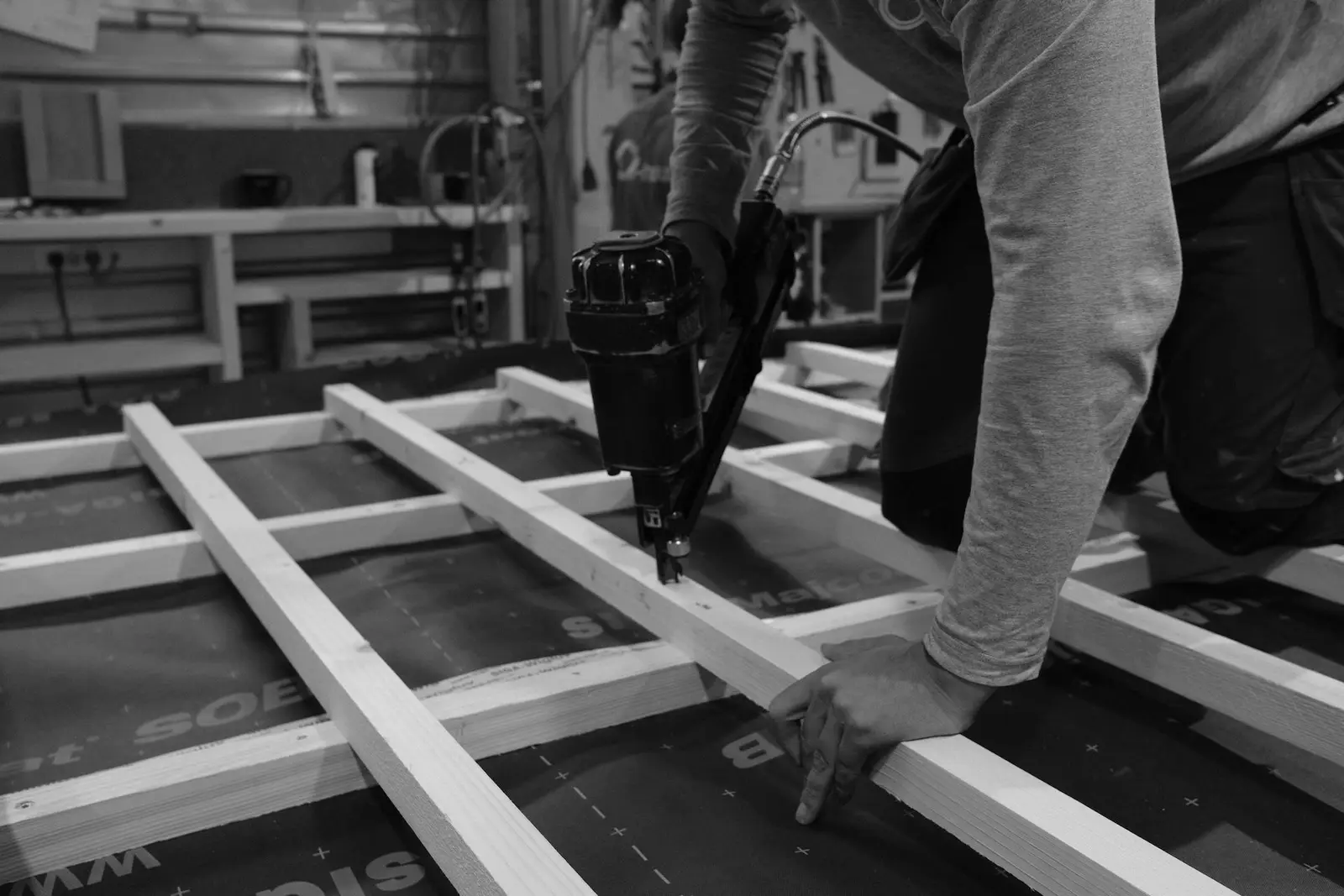 A carpenter fastens timber battens over the airtight membrane of a prefabricated wall element with a nail gun