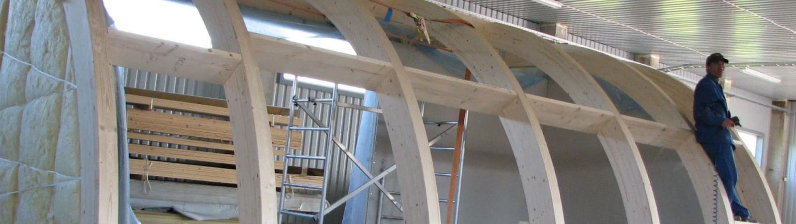 Curved glulam roof cassettes being insulated inside the factory, a carpenter checking the framing